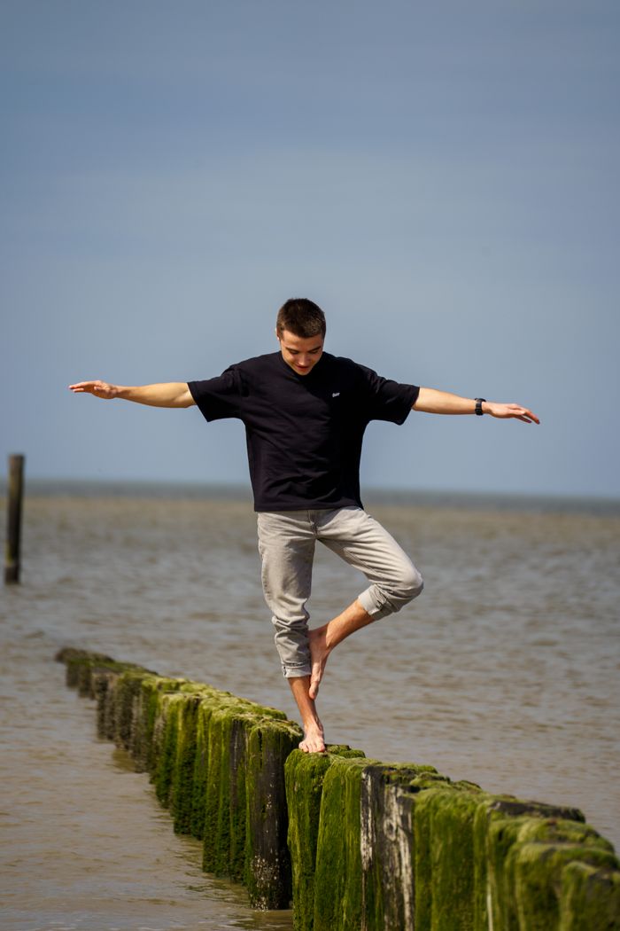 A man skillfully balances on a moss-covered wooden breakwater by the sea.